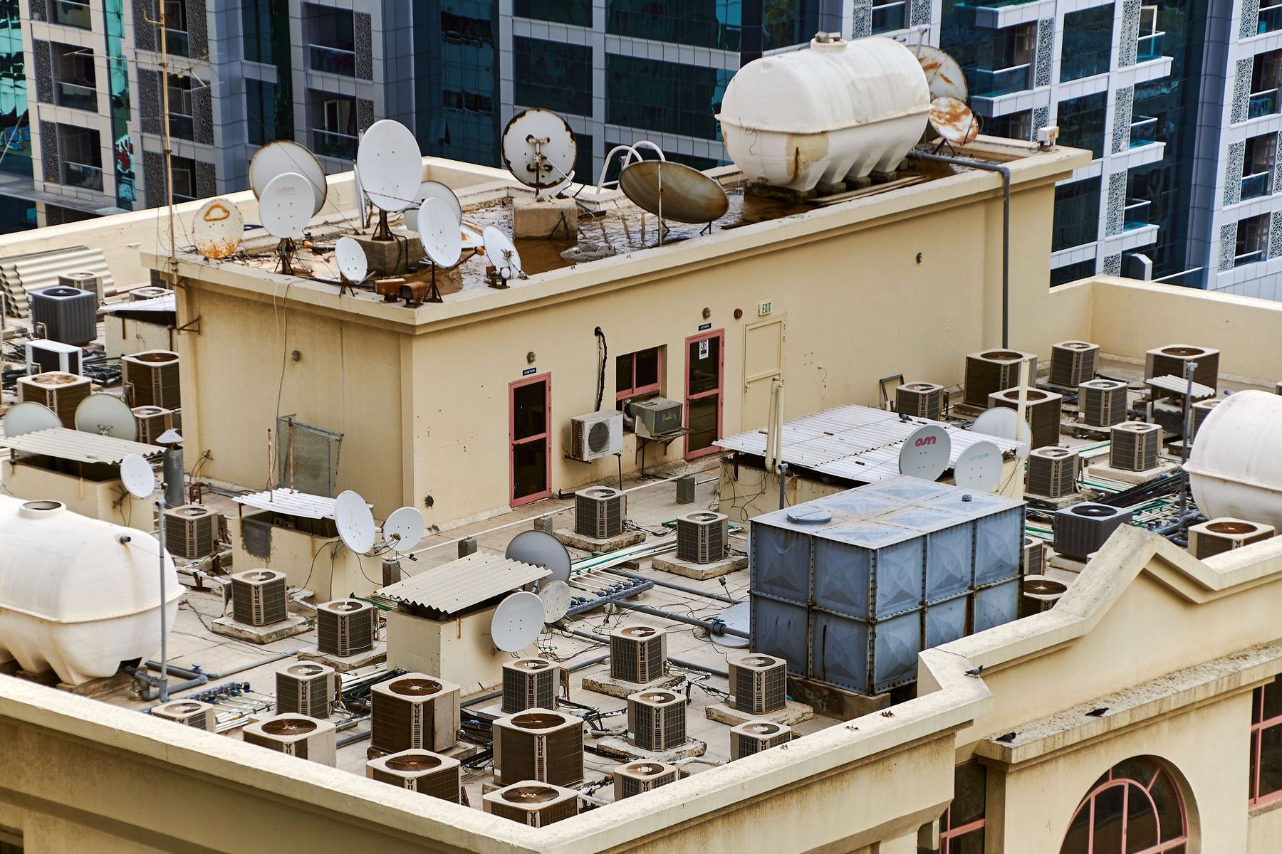 Commercial rooftop packed with HVAC condenser units, satellite dishes, and water tanks.
