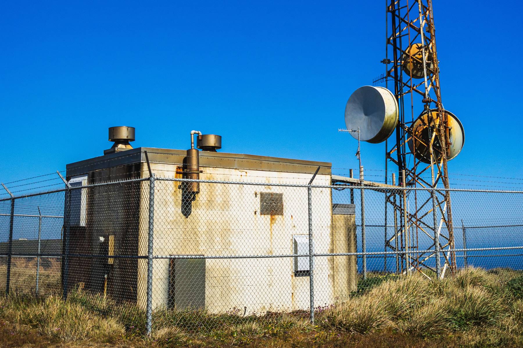 Fenced telecommunications site with an equipment building and a lattice tower with microwave dishes.